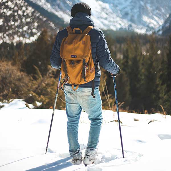 Un homme équipé de baton de ski sur une montage enneigé porte un sac à dos élégant et chic en cuir