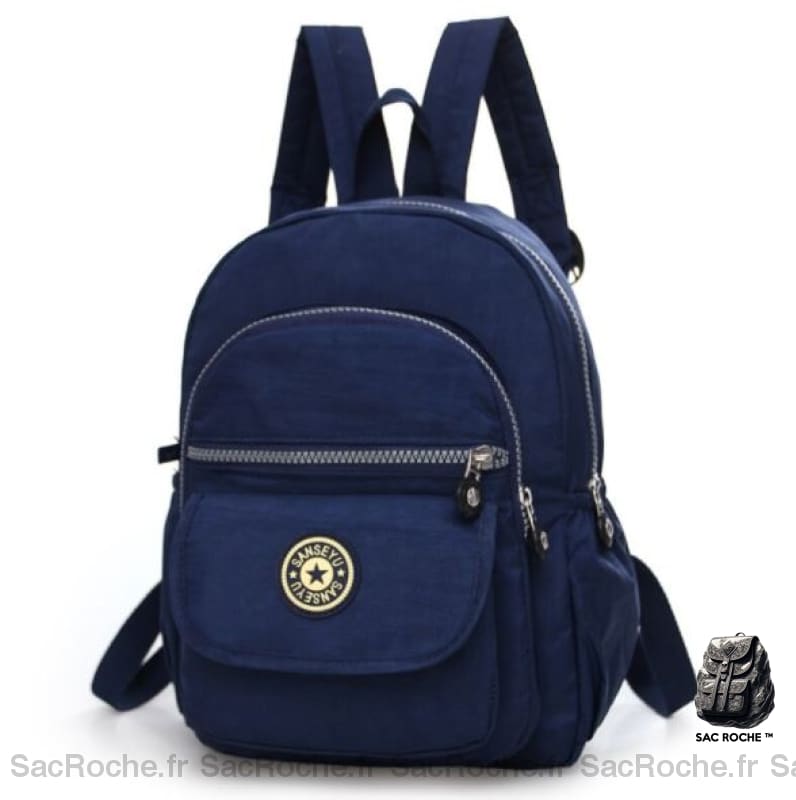 Mini sac à dos pour femme étanche de couleur unie bleu marine. Le sac à dos a quatre poches de tailles différentes. Une avec un velcro et 3 avec des zips. Sur la poche avec le velcro, il y a le logo du sac. Le sac a une hanse pour le tenir sur un crochet et deux hanses pour pouvoir le porter sur le dos.