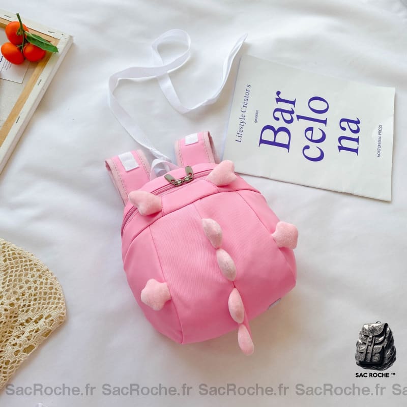 Sac à dos préscolaire forme dinosaure rose avec un fond blanc et un poster avec des écritures bleu